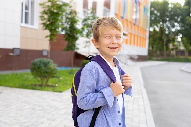 Un écolier se tient avec un sac à dos près de l'école sourit rit école primaire