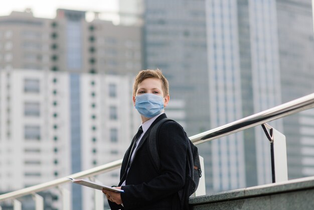 Un écolier sort de l'école avec un masque de protection dans la ville