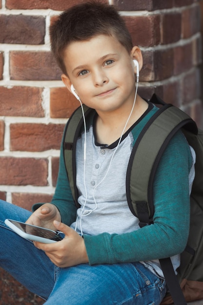 Un écolier souriant écoute de la musique sur un casque est assis avec un téléphone dans les mains