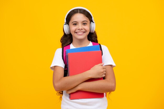 Une écolière adolescente dans un casque tient des livres sur fond de studio isolé jaune