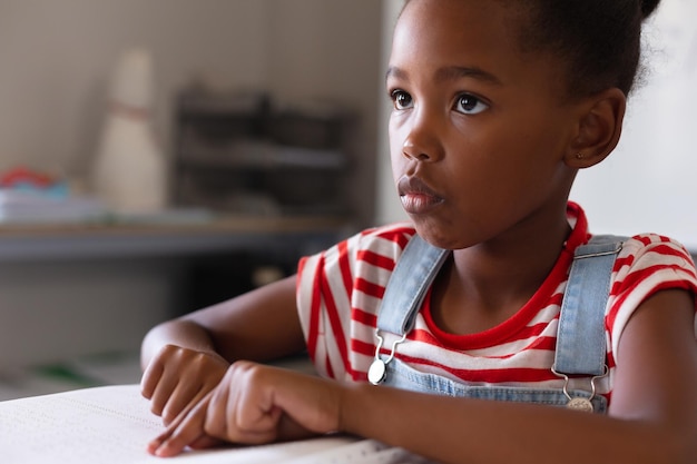 Une écolière afro-américaine détournant les yeux pendant qu'elle étudie un livre en braille en classe.