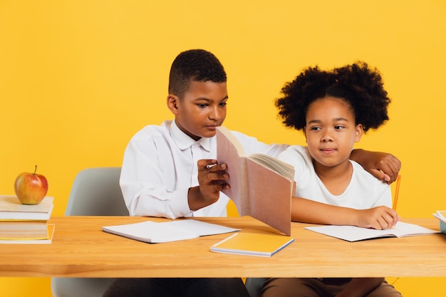 Une écolière afro-américaine heureuse et un écolière assis ensemble à un bureau et étudiant sur le jaune