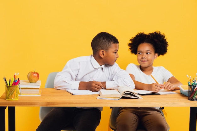 Une écolière afro-américaine heureuse et un écolière assis ensemble à leur bureau et étudiant.