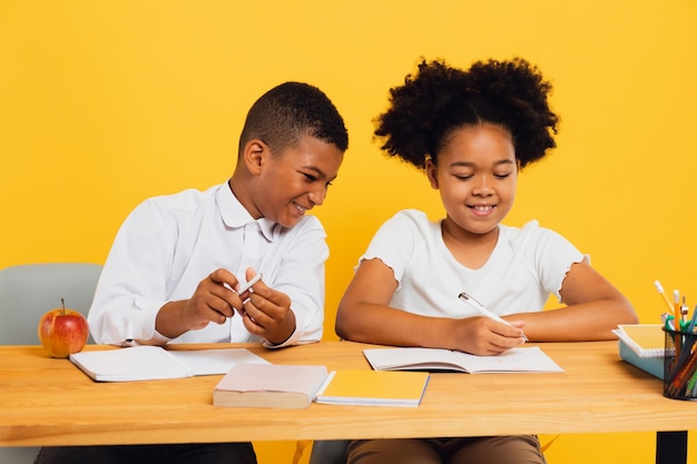 Une écolière afro-américaine heureuse et un écolière assis ensemble à leur bureau et étudiant.