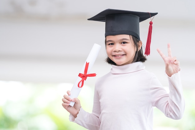 Photo une écolière asiatique diplômée d'une casquette de remise des diplômes détient un papier de certificat roulé