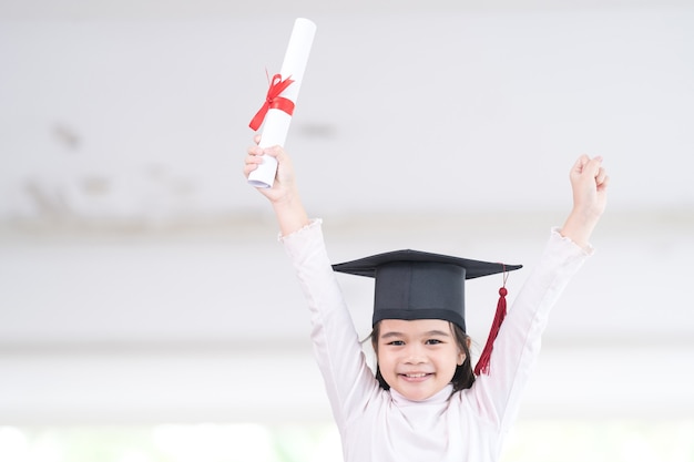 Une écolière asiatique diplômée d'une casquette de remise des diplômes détient un papier de certificat roulé