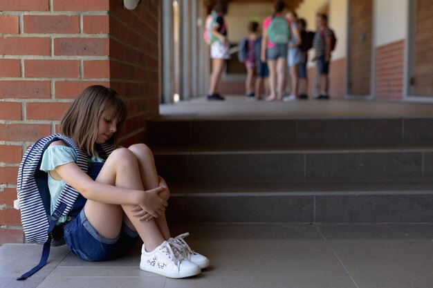 Photo Écolière assise par terre seule dans la cour de l'école primaire