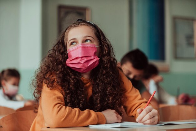 Une écolière caucasienne portant un masque facial étudie en classe