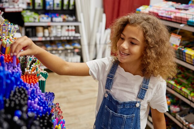 Une écolière choisit un stylo dans un magasin de papeterie pour la nouvelle année scolaire.