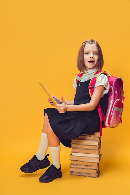 Une écolière émotionnelle pleine longueur s'assoit sur la pile de livres travaille sur le concept d'éducation des enfants sur tablette