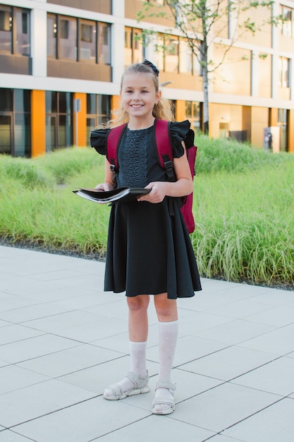 Photo Écolière fille avec un dossier dans ses mains près de l'école