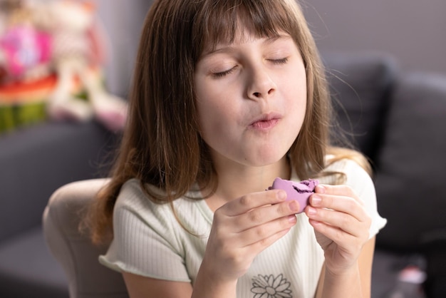 Une écolière sur un fond de maison se lèche les lèvres en mangeant un macaron violet ferme les yeux