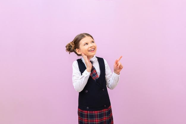 Une écolière sur fond violet pointe son doigt vers votre publicité ou votre annonce et sourit en étudiant à l'espace de copie de l'école