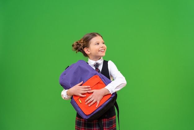 Une écolière gaie avec une mallette dans ses mains Une fille en uniforme scolaire sur un fond vert isolé