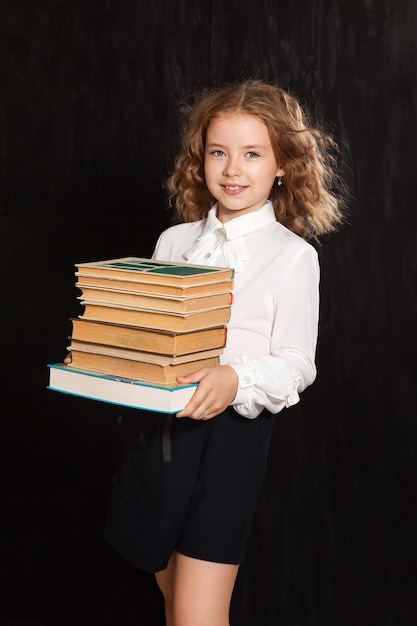 Une écolière heureuse tient des livres et des manuels sur fond noir