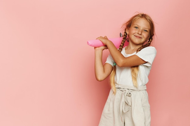 Une écolière joyeuse avec une jolie coiffure apprécie l'été en mode rose.