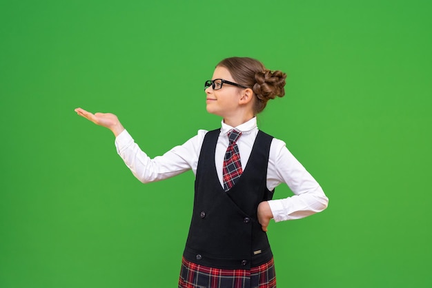 Une écolière joyeuse tient votre publicité sur sa main. Une petite fille en uniforme scolaire pointe du doigt une publicité.