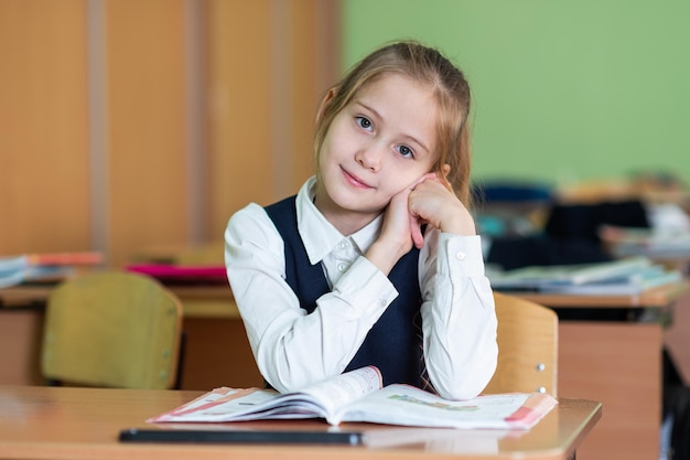 Une écolière mignonne est assise à un bureau entouré de livres Regarde dans la caméra La vie de l'école