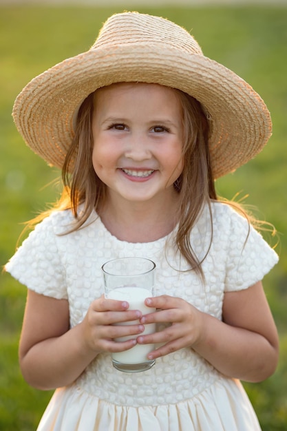 Une écolière de première année au chapeau boit du lait en souriant