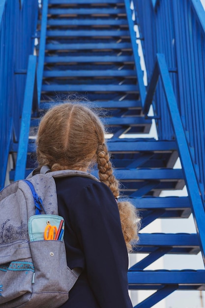 Photo Écolière regardant les escaliers jours d'école conceptuels date de début étape suivante échelle de carrière le début du chemin fille en uniforme avec un sac à dos fille près des escaliers