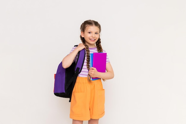 Une écolière avec un sac à dos scolaire et des livres dans ses mains sur un fond blanc isolé Éducation pour les enfants