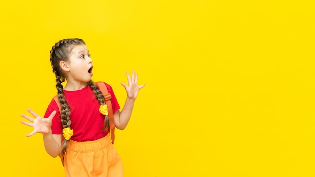 Une écolière avec une sacoche regarde votre publicité pour des cours éducatifs pour écoliers Une petite fille se prépare aux examens sur un fond jaune isolé Copiez l'espace