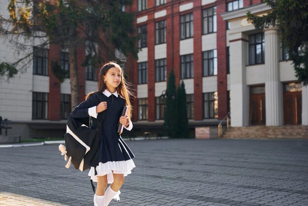 Une écolière se promène à l'extérieur près du bâtiment de l'école