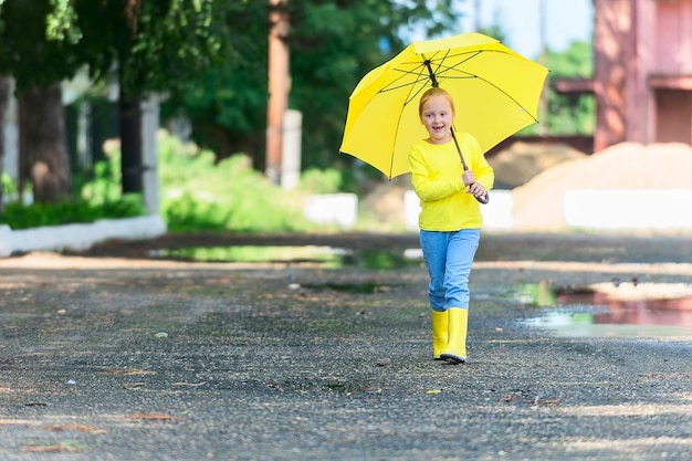 Une écolière de sept ans avec un parapluie dans les mains, en bottes de caoutchouc pour une promenade