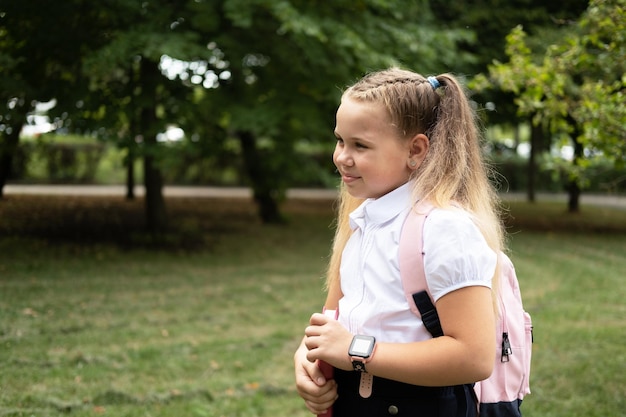 écolière souriante blonde en uniforme scolaire tenant un cahier avec sac à dos rose retour à l'école