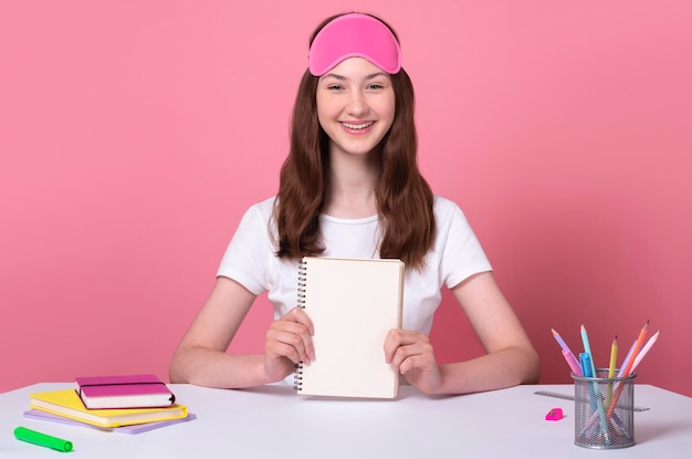 Une écolière souriante et joyeuse montre un espace de copie pour ordinateur portable isolé sur fond rose