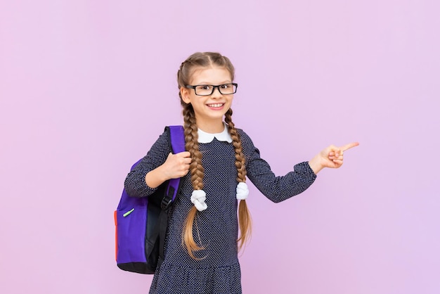 Une écolière souriante pointe son doigt sur le côté de la publicité Une fille en uniforme scolaire sur un fond isolé