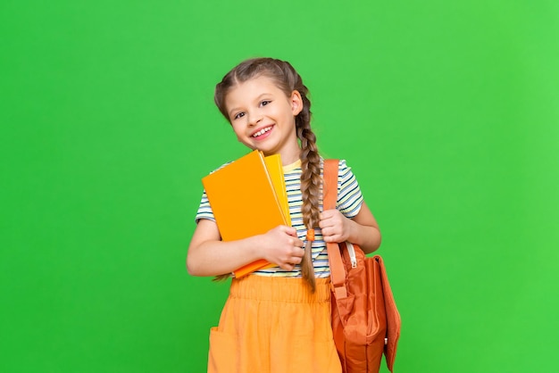 L'écolière tient des manuels et sa mallette d'école et est très heureuse. Une fille sur un fond isolé avec espace de copie.