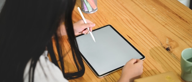 Une écolière utilise une tablette informatique à écran blanc et un stylet dans le salon.