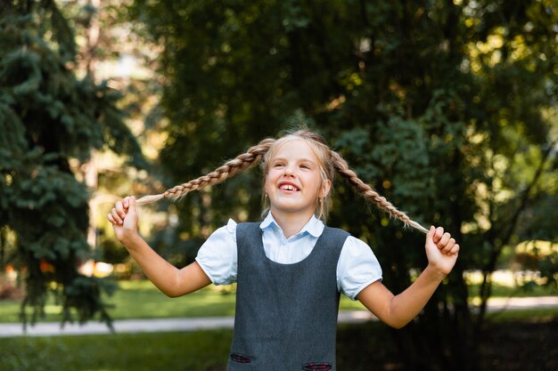 Une écolière va à l'école avec les mains levées sur le fond du parc. fille en uniforme scolaire dans le parc.