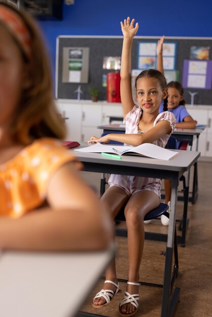 Photo des écoliers élémentaires divers lèvent la main à leur bureau en classe.