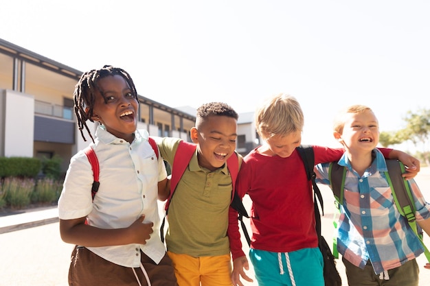 Des écoliers élémentaires multiraciaux joyeux se tiennent debout sur le campus de l'école par une journée ensoleillée.