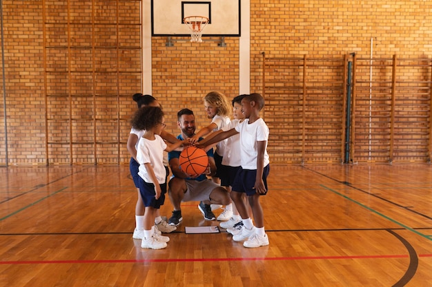 Des écoliers et un entraîneur de basket-ball s'accrochent aux mains sur le terrain de basketball à l'école.