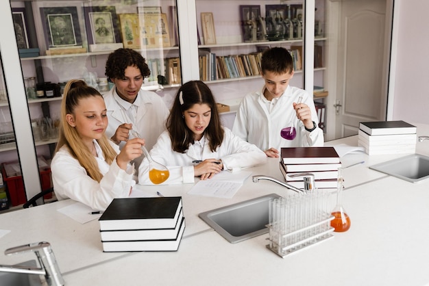 Les écoliers étudient à la leçon de chimie en classe Les élèves écrivent dans un cahier tenant des flacons avec du liquide pour des expériences et s'amusent ensemble Éducation scolaire