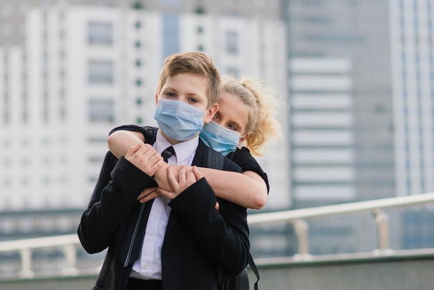 Des écoliers, un garçon et une fille portant des masques médicaux marchent dans la ville.