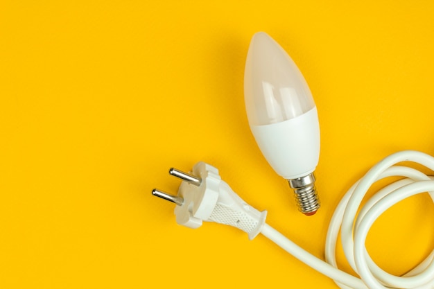 Photo Économie d'énergie, concept écologique. ampoule led et câble d'alimentation électrique avec prise ue, fond jaune, vue de dessus et mise à plat avec photo de l'espace de copie