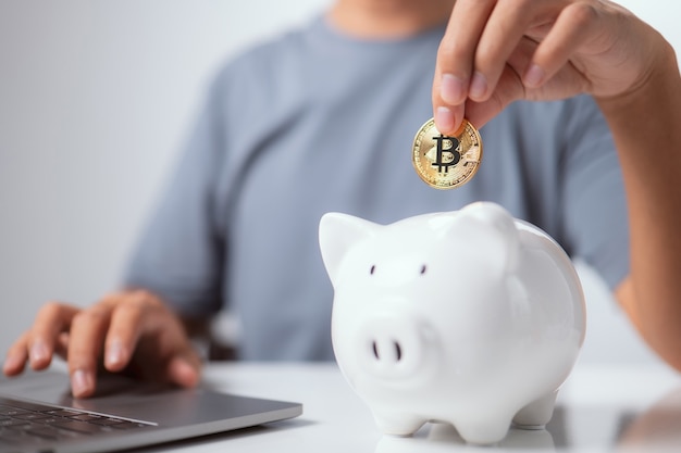 Économies commerciales et financières L'homme met le bitcoin Golden Cryptocurrency dans une tirelire blanche