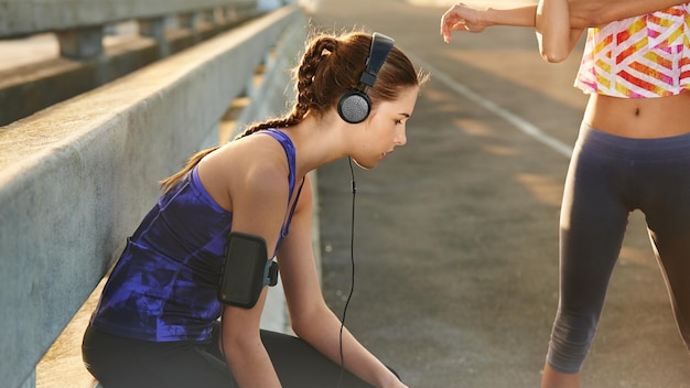 Les écouteurs de fille et le coureur se détendent en ville en étirant les bras et en diffusant de la musique pour l'échauffement cardio La personne féminine se repose et la rue urbaine pour l'entraînement bien-être de la ville et écoute le podcast audio