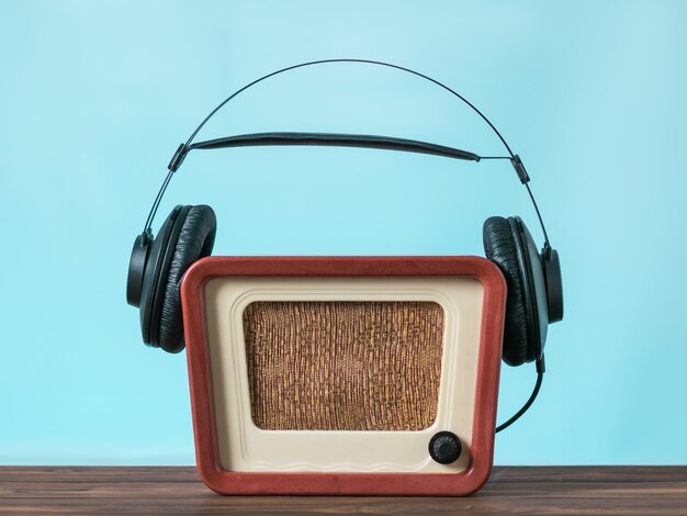 Des écouteurs noirs sont portés sur un moniteur vintage sur une table en bois sur fond bleu. Technique de reproduction sonore et vidéo.