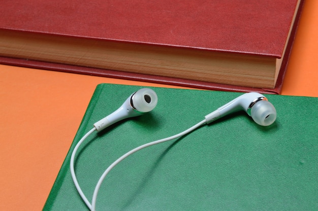 Photo des écouteurs à vide blancs se trouvent sur des livres disposés sur un papier orange