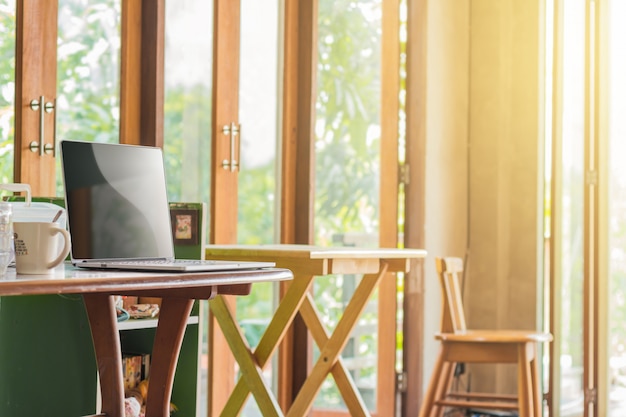 Photo Écran blanc d'ordinateur portable sur un bureau en bois et une chaise à l'intérieur de la chambre avec la lumière du matin