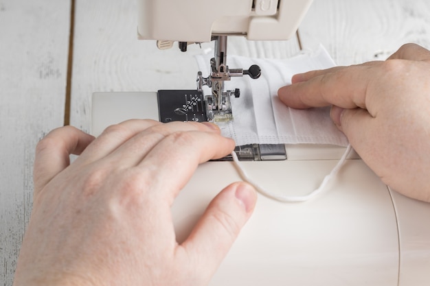 Un écran facial jetable et un masque multi-visage fait maison se trouvent sur la machine à coudre, faites-vous un masque de protection à partir du tissu à la maison, masque de protection à faire soi-même