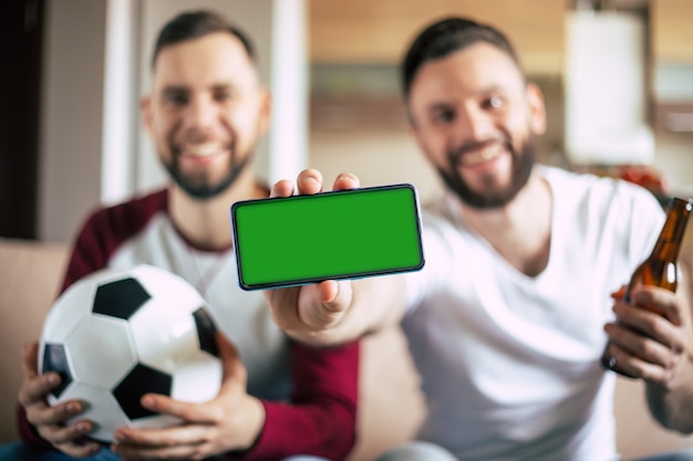 écran vert sur le smartphone dans la main de jeunes amateurs de sports barbus excités. Gagner aux paris