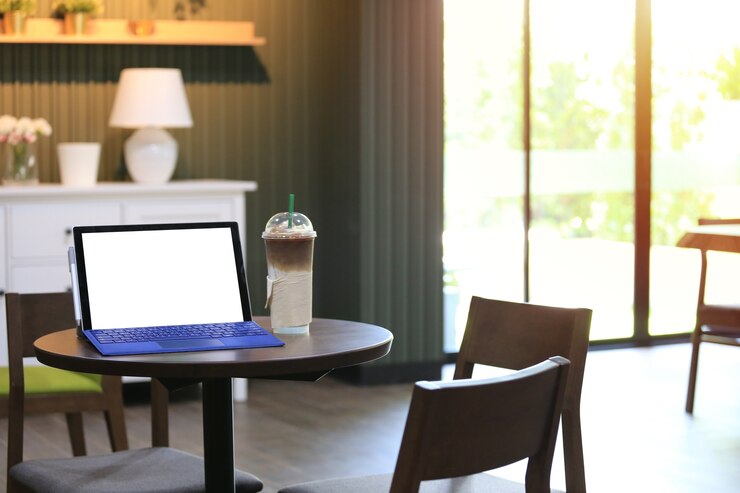 Écran vide d'un ordinateur portable et d'une tasse de café froide placée sur une table de nourriture dans un café.
