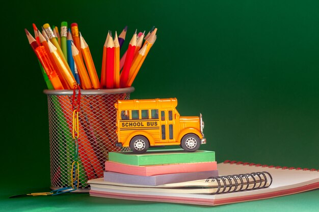 L'éducation et le concept de retour à l'école. Autobus scolaire rétro jaune et crayons dans le panier, manuels sur vert foncé