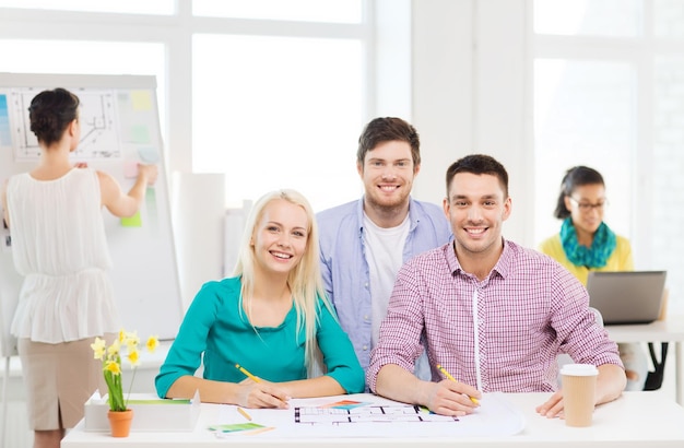 éducation, design d'intérieur et concept de bureau - designers d'intérieur souriants avec des échantillons de couleurs et des plans au bureau